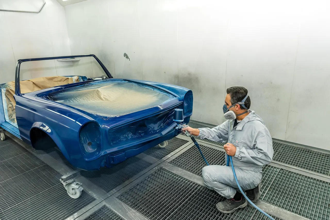 Spray painter refinishing a car in a booth